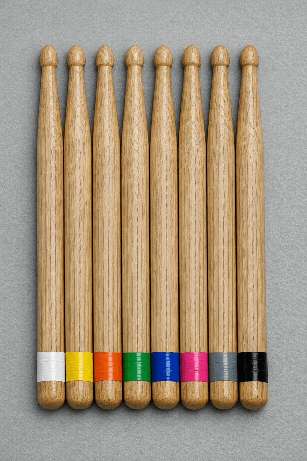Eight drumsticks with colored tape rings in order: white, yellow, orange, green, blue, pink, gray, black lined up close together.